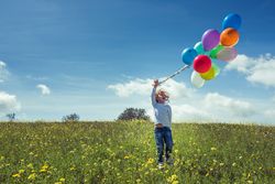 Excited kid holding balloons in grassy countryside