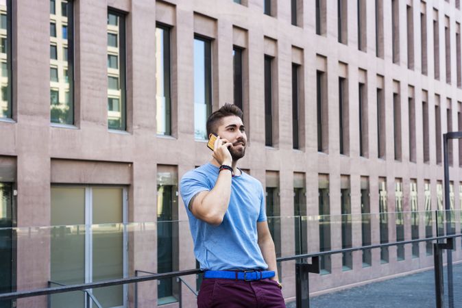 Portrait of cheerful modern businessman speaking by phone leaning outside