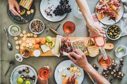 Charcuterie board with hands pouring glass of rose and reaching for cheese