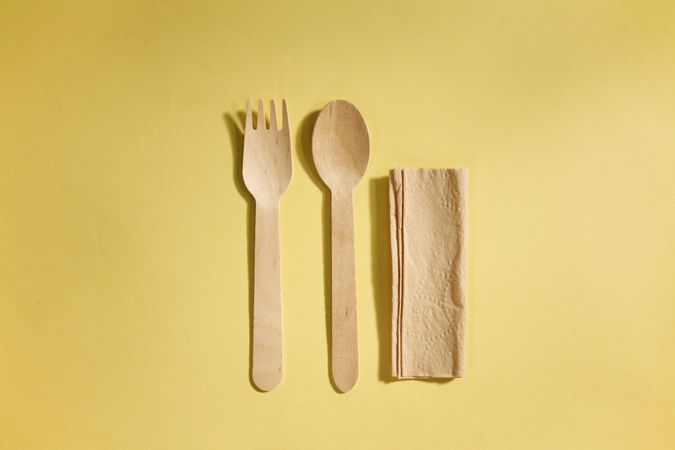 Disposable fork, spoon and napkin on yellow background
