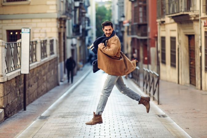Happy man jumping in middle of street in jeans and jacket