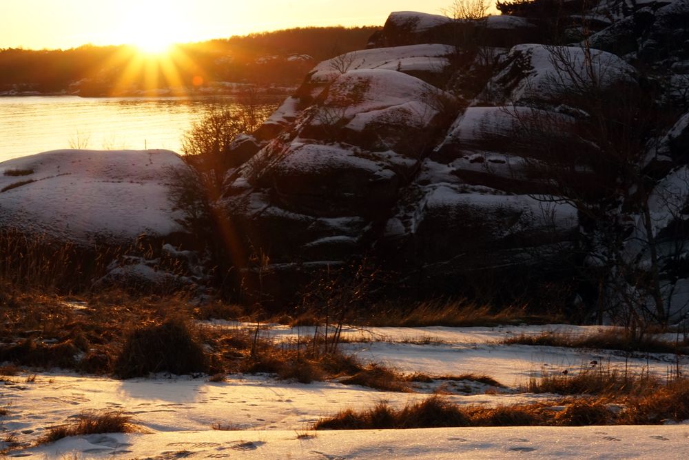 Rocky peaceful shore with snow crust in sunrays