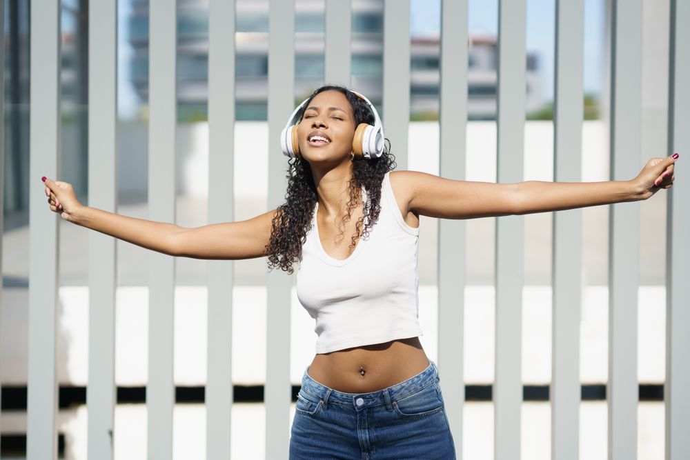 A Joyful Young Woman Expressively Dancing with Headphones in a Vibrant Outdoor Setting