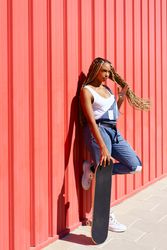 Woman leaning against red wall with skateboard, vertical composition