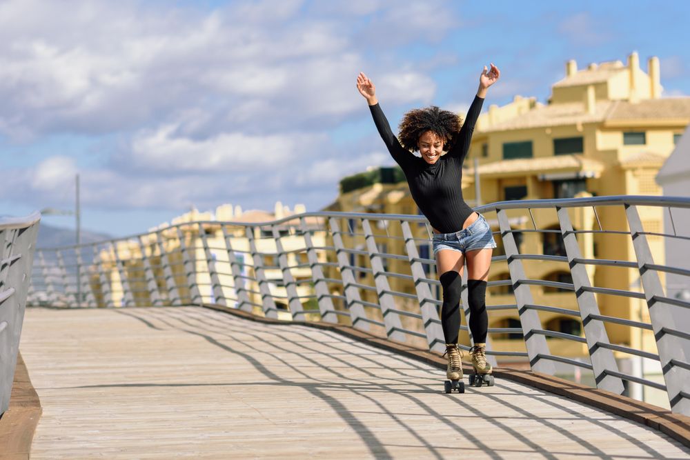 Smiling woman with afro hairstyle rollerblading on wooden bridge