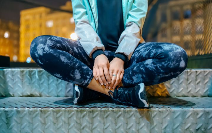 Unrecognizable female athlete sitting with cross legged on metallic staircase at night