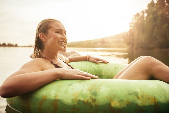 Portrait of happy young woman in lake on inflatable ring looking away and smiling