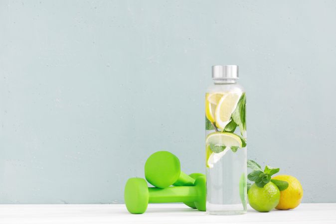 Dumbbells and fresh water with citrus on baby blue background