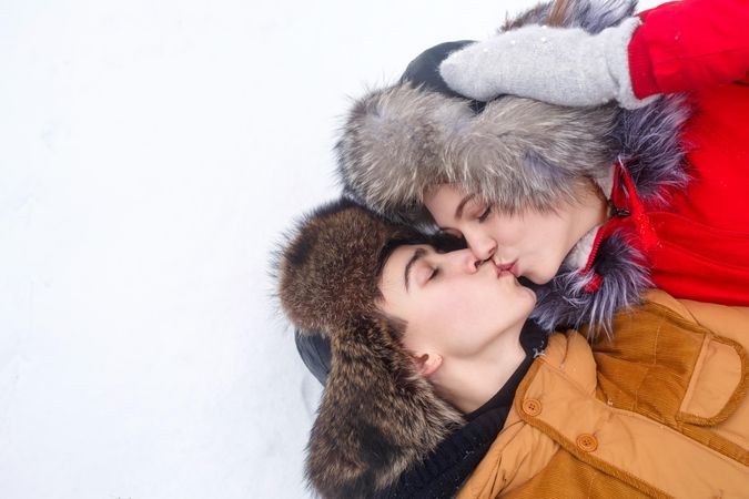 Teenage couple lying in snow together and kissing