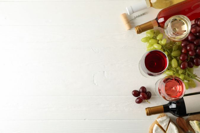 Grape, cheese, bottles and glasses with different wine on light wooden background, copy space