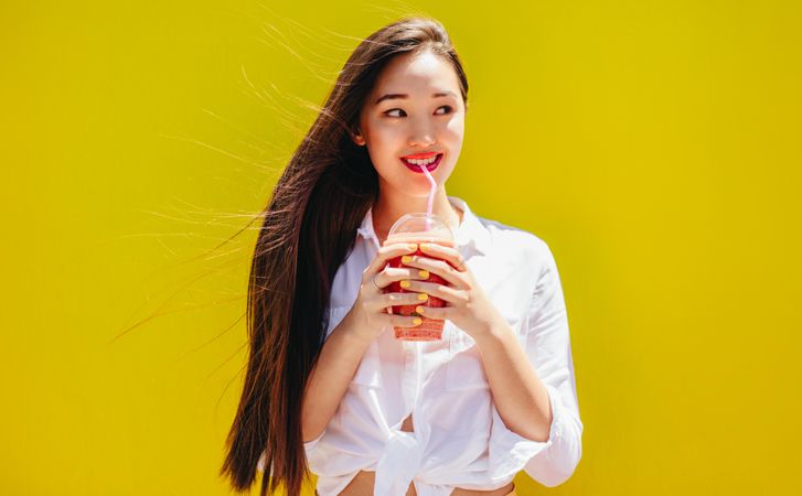 Cheerful young woman holding a cup of juice and looking away