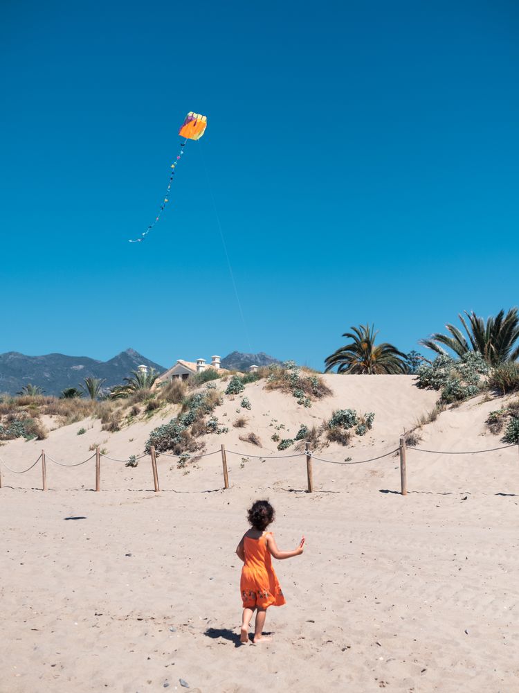 Toddler girl playing with kite on sandy beach