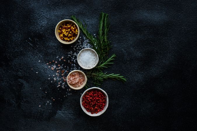 Top view of salt and seasoning bowls and rosemary on kitchen counter with copy space