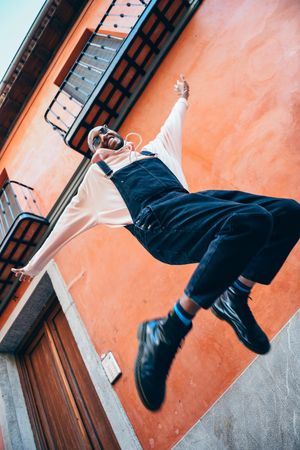 Jumping male in overalls and hoodie looking down at camera