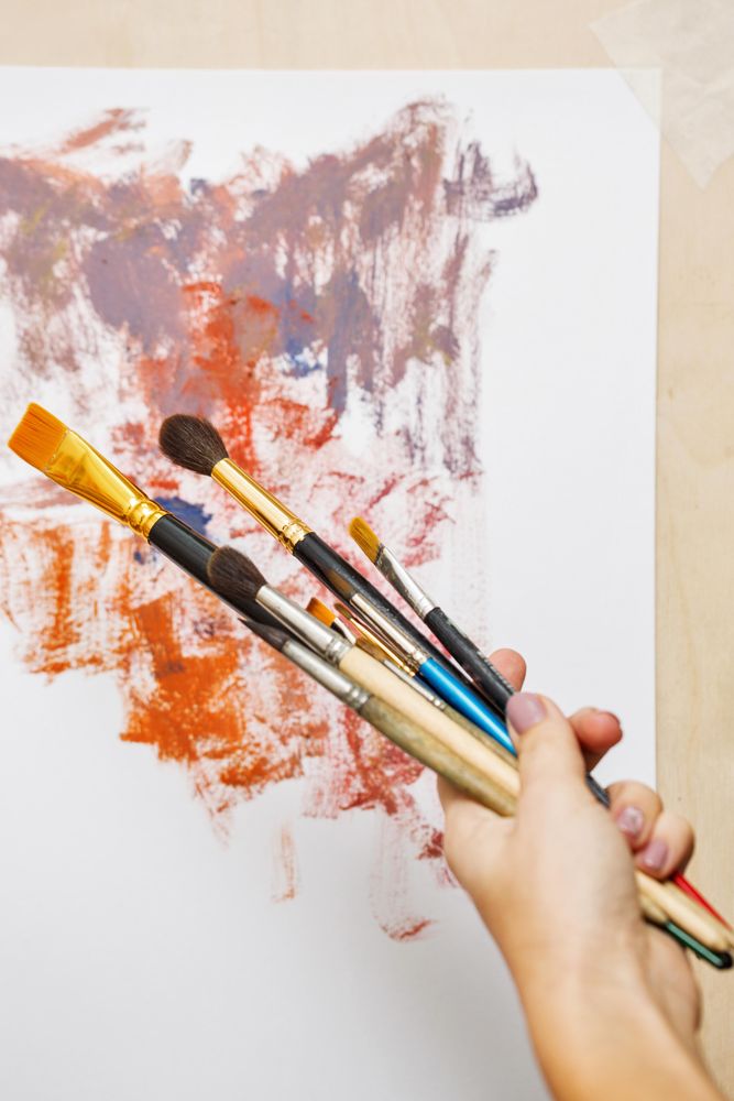 Hand holding paint brushes in front of painting