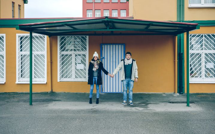 Couple holding hands under a metallic roof outdoors in a cold and rainy autumn day