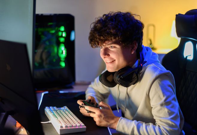 Concentrated happy young man sitting before monitor and playing games with joystick