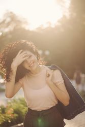 Smiling woman looks tat camera while holding coat over shoulder