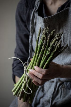 Faceless woman holding bundle of green asparagus