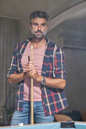 Pensive bearded man standing with cue