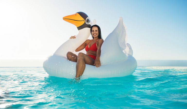 Beautiful woman sitting on inflatable pool toy at a resort infinity pool