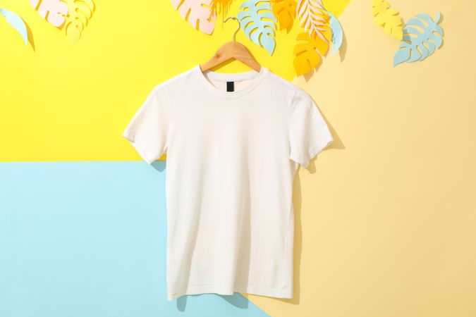 Hanger with blank plain t-shirt on multicolored background, space for text