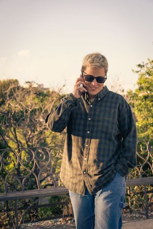 Young person with short blonde hair talking on a smartphone outdoors at sunset.