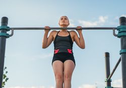 Female athlete doing pull ups on a bar outdoors, calisthenics