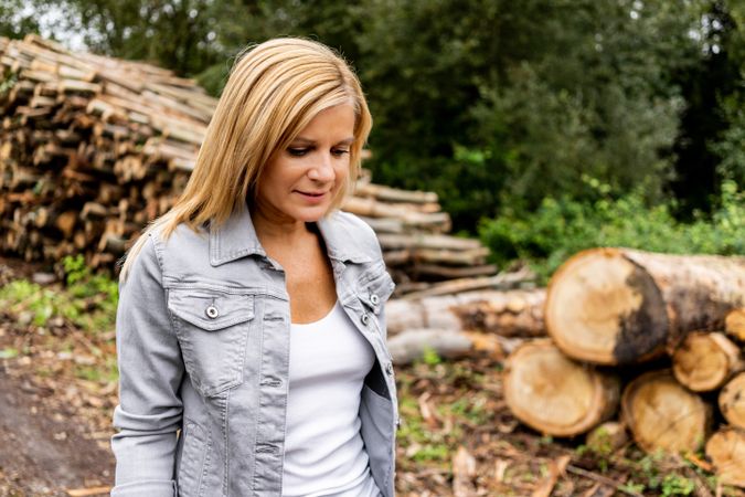 Woman taking off jacket on background of woodpile in forest
