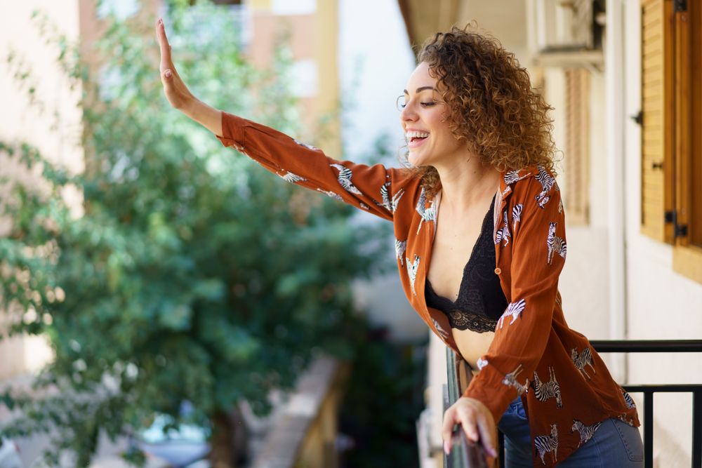Smiling woman waving down at street from her balcony