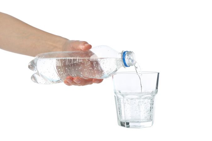 Hand pouring water in glass from plastic bottle in plain studio