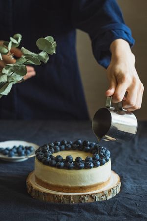 Person pouring honey on top of blueberry cheesecake