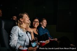 Friends sitting in movie theater with popcorn and drinks 56xPYb
