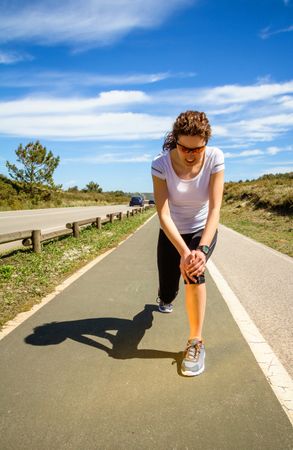 Woman in athletic gear doing lunges to stretch next to road