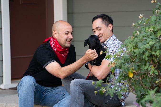 Two men smiling at their dog while sitting on their front porch after work
