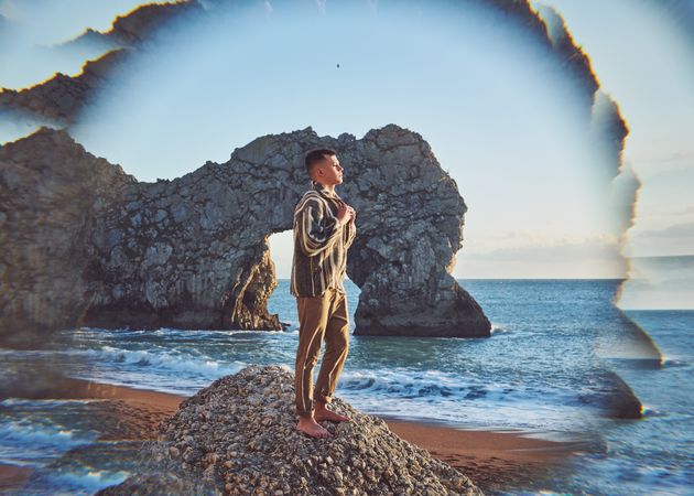 Young man standing on rock mound at the beach on a clear day with sea cliff in background