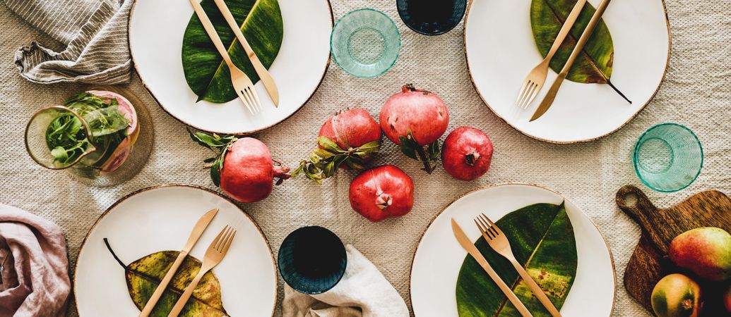 Fresh table setting on brown table cloth, leaves on bright plates, pomegranate, wide composition