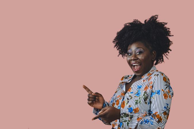 Studio shot of joking Black woman in floral print shirt pointing her fingers
