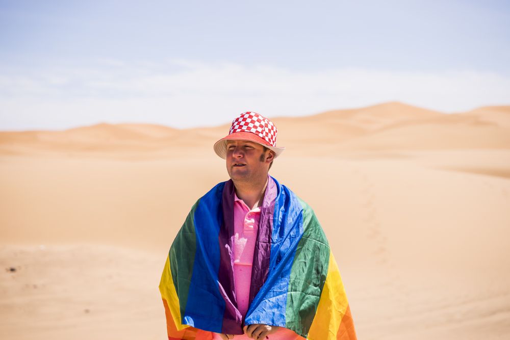Gay man wrapped in rainbow flag standing in desert