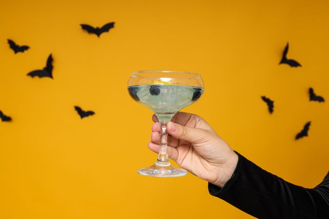 Cocktail in hand, on a yellow background with bats