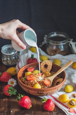 Person pouring milk into bowl with granola and fruit