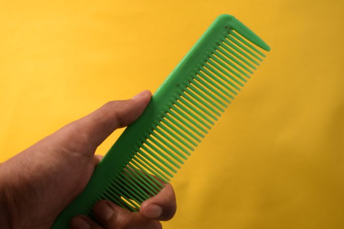 Hand with green hair comb in yellow studio