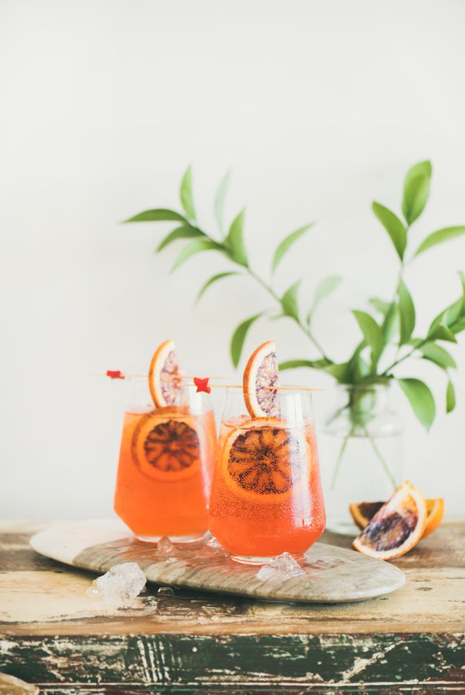 Two glasses of an orange cocktail with orange slices, and leaves in background, with copy space