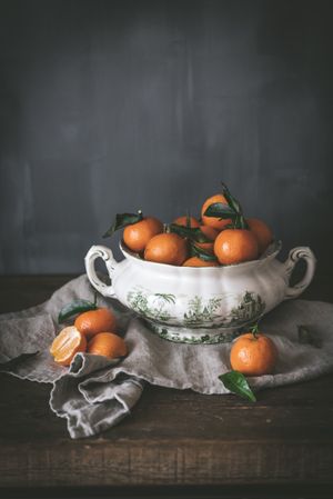 Orange tangerines in ceramic ornamental bowl on wooden table