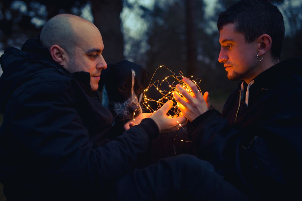 Men holding fairy lights near dog in forest at night