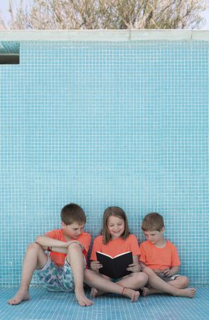 Children sitting in empty pool and reading book