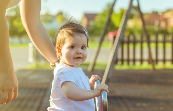 Baby girl playing over a seesaw swing on the park