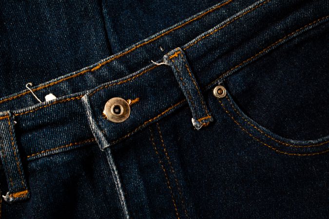 Close up gold and shiny button navy blue jeans fabric background texture.