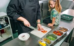 Unrecognizable chef teaching little girl how to prepare healthy poke bowl in a professional kitchen