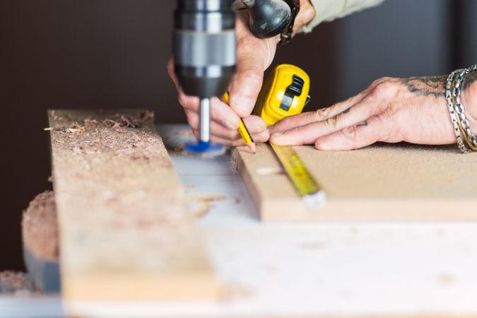 Unrecognizable male carpenter measuring wooden plank at workbench